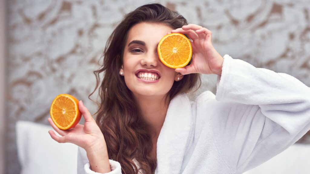 Mulher mostrando uma laranja representando a ajuda no cescimento capilar